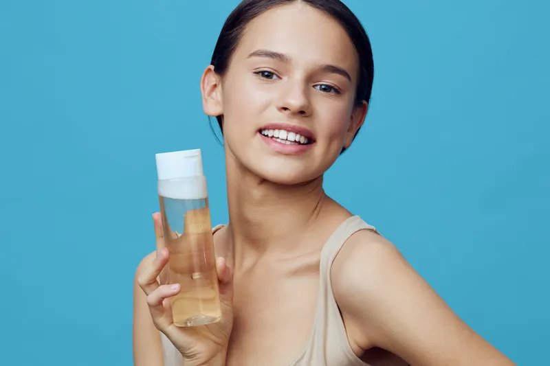 Young woman holding a beauty product with a joyful expression against a vibrant blue background, showcasing skincare and self care concepts