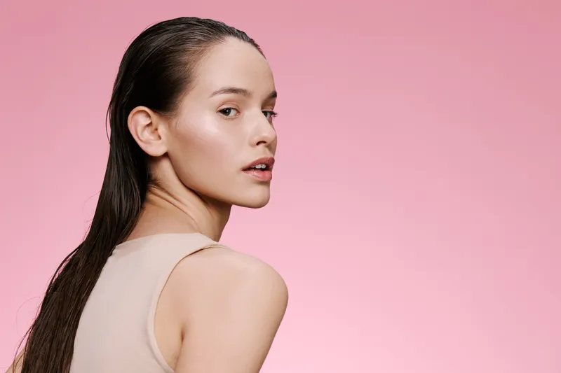 Portrait of a young woman with long hair, showcasing a natural look against a soft pink background, embodying beauty and elegance in a fashion forward style