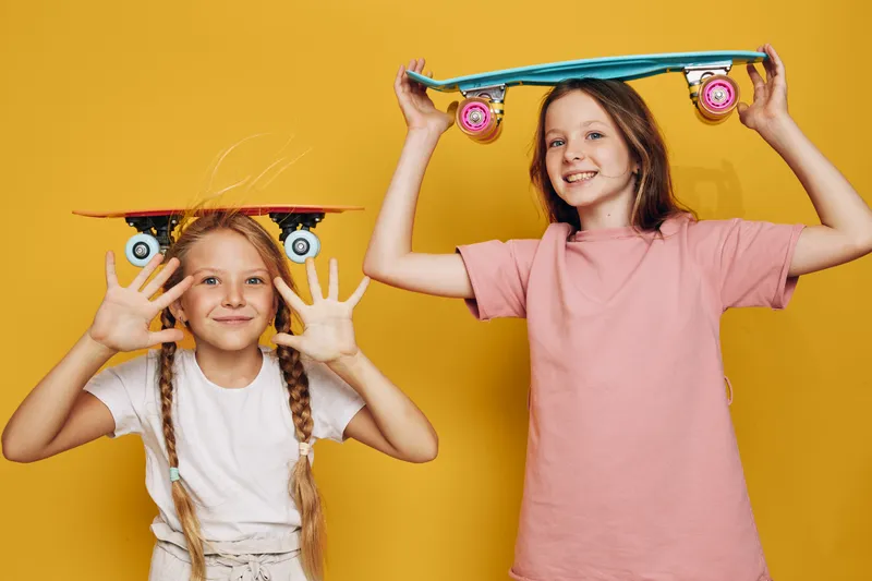Two happy girls posing with skateboards, smiling and having fun on a yellow background. Concept of childhood, play, and active lifestyle.
