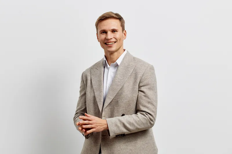 Smiling man in smart casual attire posing confidently against plain light gray background, friendly expression, modern style, professional look, studio portrait, lifestyle concept