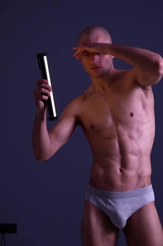 Strong man posing confidently with a light stick against a dark background, showcasing physical fitness and strength. Captivating black and white imagery.