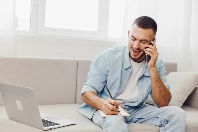 Engaged man communicating over the phone while jotting notes, embodying emotional minimalism and the concept of solo living in a modern workspace.