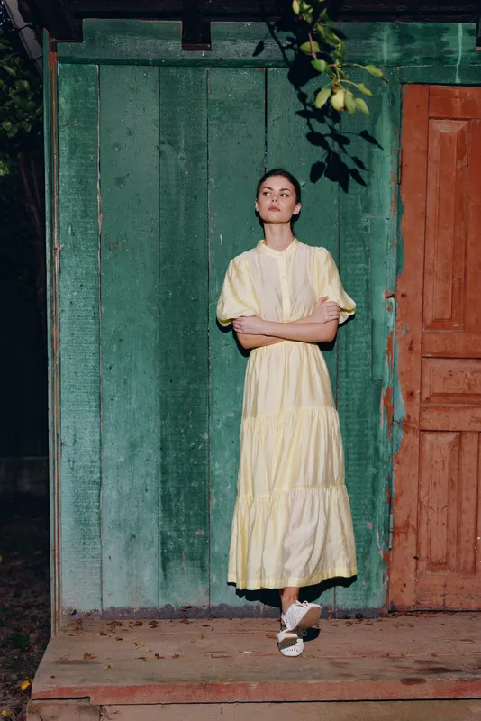 Woman dress portrait standing wooden vintage authenticity inclusivity by weathered green wall and door, yellow dress, natural light, calm rural scene