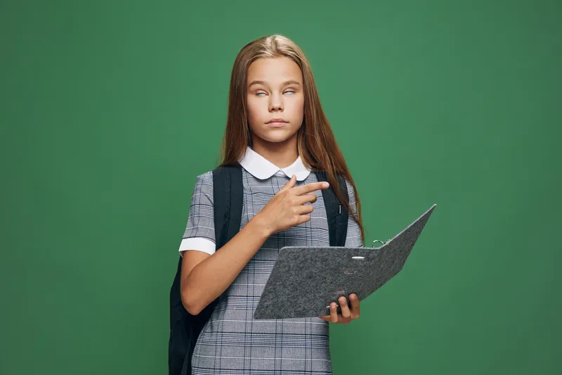 Girl student holding folder and pointing with finger on green background, wearing backpack and school uniform for education and knowledge concept.