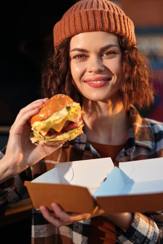 woman burger smile takeaway beanie candid street Candid lifestyle portrait of a woman eating a juicy burger at golden hour glow, authenticity, mindful living and emotional storytelling in urban