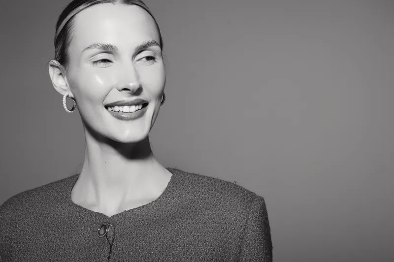 Smiling caucasian woman with light skin wearing earrings and jacket looks away on grey background. Concept of happiness and natural beauty.