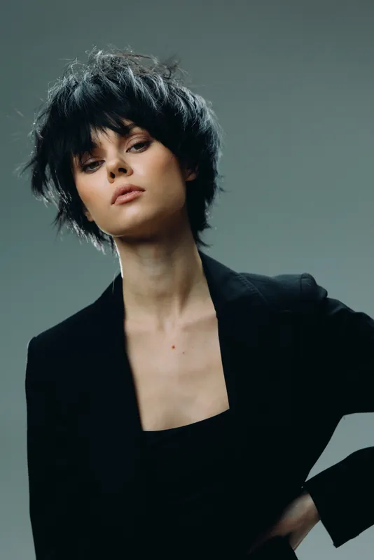 Stylish woman with short black hair wearing a black blazer looking confidently with a neutral background