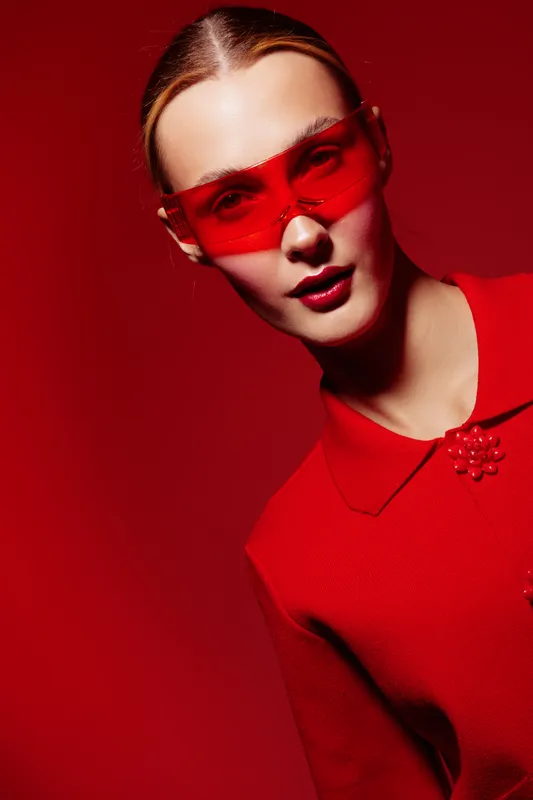 Young woman in red outfit and red sunglasses poses against red background. Fashion portrait with bold color contrast and modern style. Concept of confidence, style, and vibrant look.
