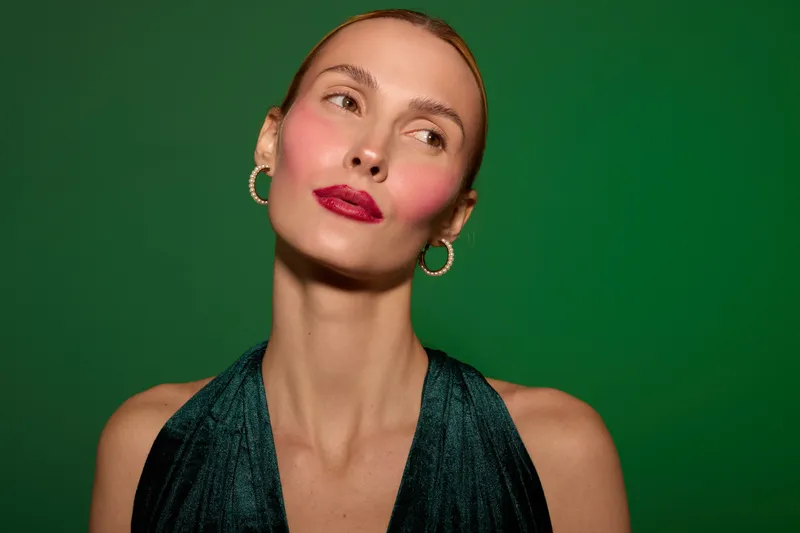 Portrait of a confident woman with red lipstick and hoop earrings wearing a dark green dress against a green background. Concept of beauty, fashion, and elegance.