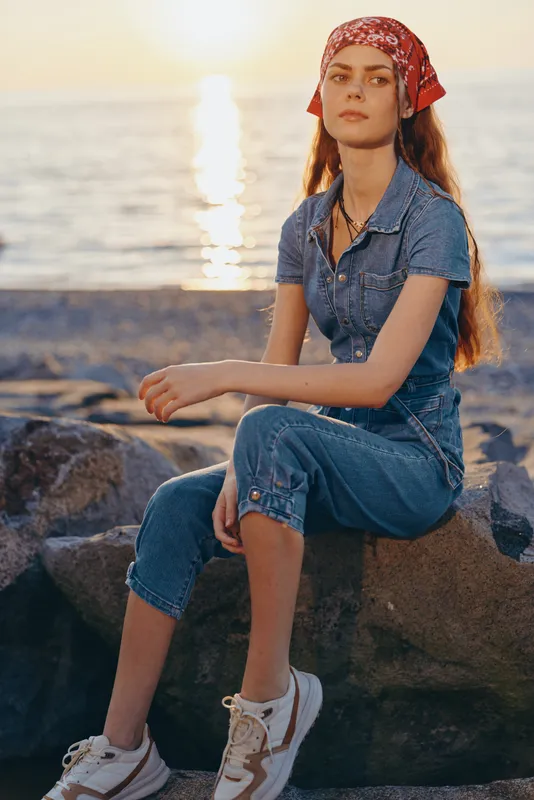 lifestyle woman wearing modern boho-western denim street style outfit sitting by sunset beach, film color vibe, relaxed mood, casual fashion look