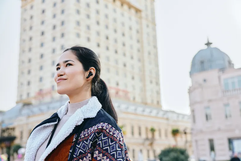 Woman in stylish jacket walks along an urban street with architecture in the backdrop, offering a cheerful mood, fashion forward look, and city ambiance