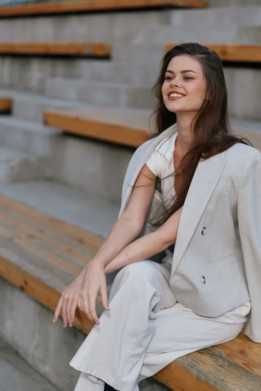 Business woman in light-colored suit smiling confidently outdoors, showcasing professionalism and modern elegance on wooden steps.