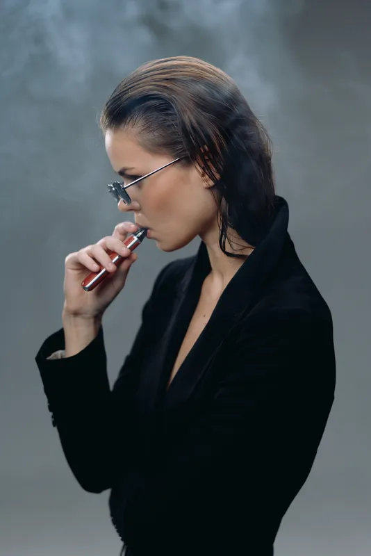 Woman vaping with electronic cigarette wearing glasses and black suit in smoky atmosphere
