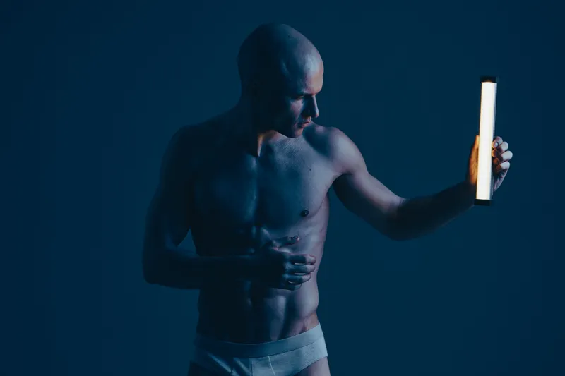 Athletic man posing in low light, showcasing body contours with dramatic illumination. This black and white image emphasizes strength and fitness.