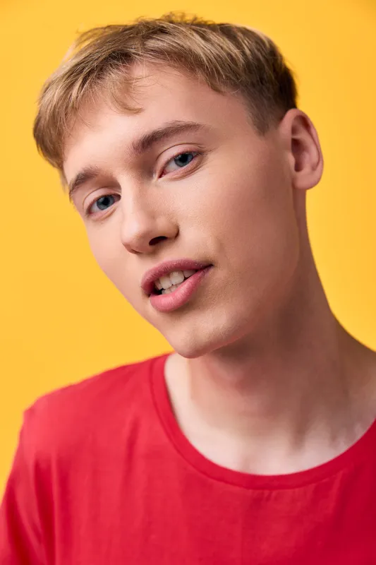Young man with a friendly smile wearing a red shirt against a bright yellow backdrop, close up shot highlighting facial features and casual fashion, modern look
