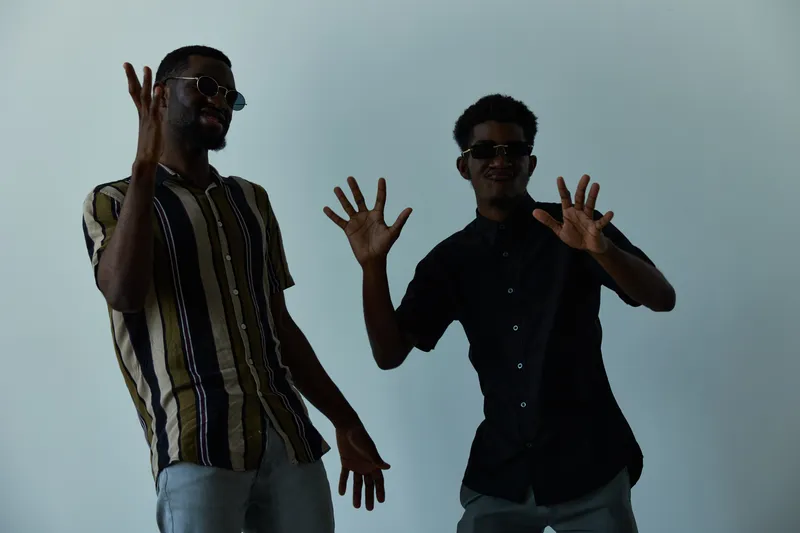 Black men expressing joy in stylish outfits, showcasing happiness and camaraderie. Vibrant energy and confidence exude from the scene, perfect for lifestyle portfolios.