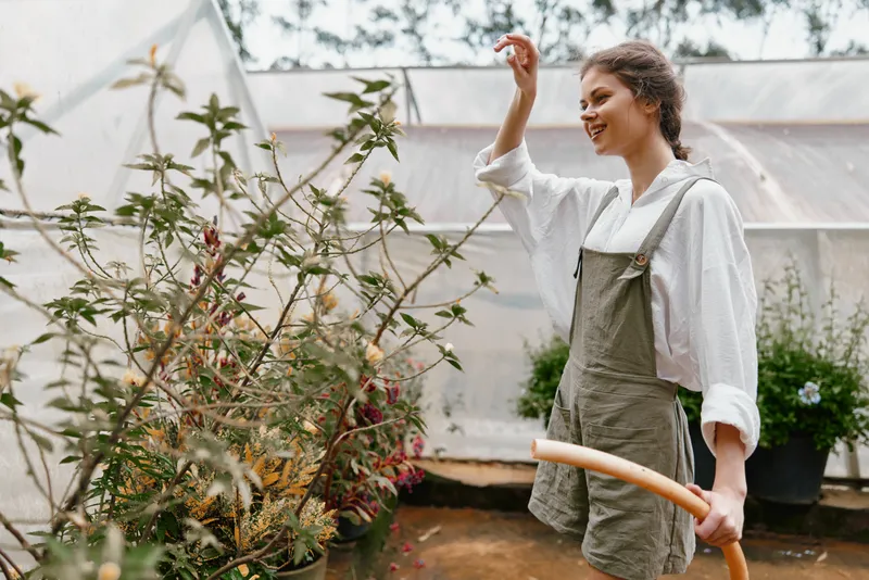 Young woman gardening in a greenhouse, wearing casual overalls and a white shirt, showcasing joy and a connection to nature A vibrant green background adds freshness