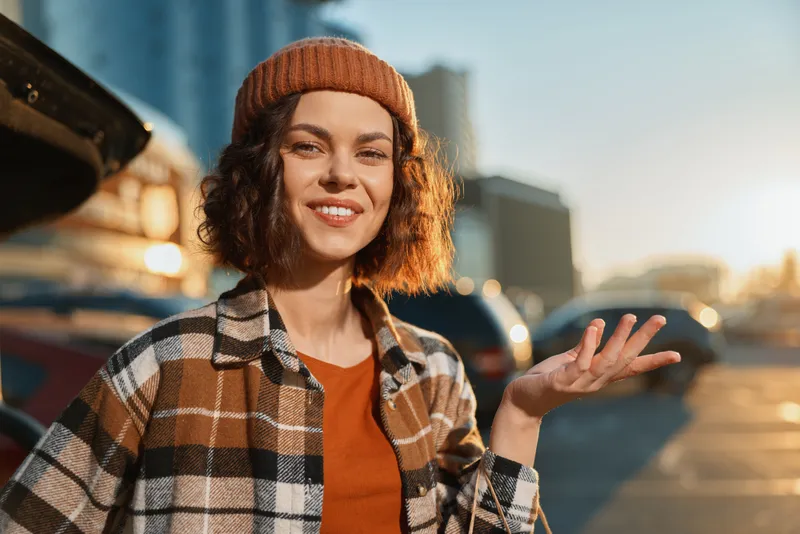 Woman smile urban candid lifestyle beanie golden sunset authenticity mindful living emotional storytelling. Young curly-haired woman in city street laughing with warm golden hour glow and relaxed