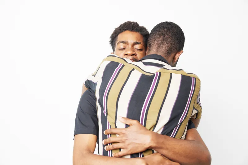 Embracing black men share a heartfelt moment, showcasing love, unity, and connection in a joyful atmosphere. The composition highlights their emotional bond beautifully.