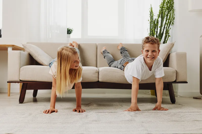 Two happy children doing push ups on carpet in bright living room, smiling boy and girl exercising together at home. Concept of fitness, childhood activity, and healthy lifestyle.