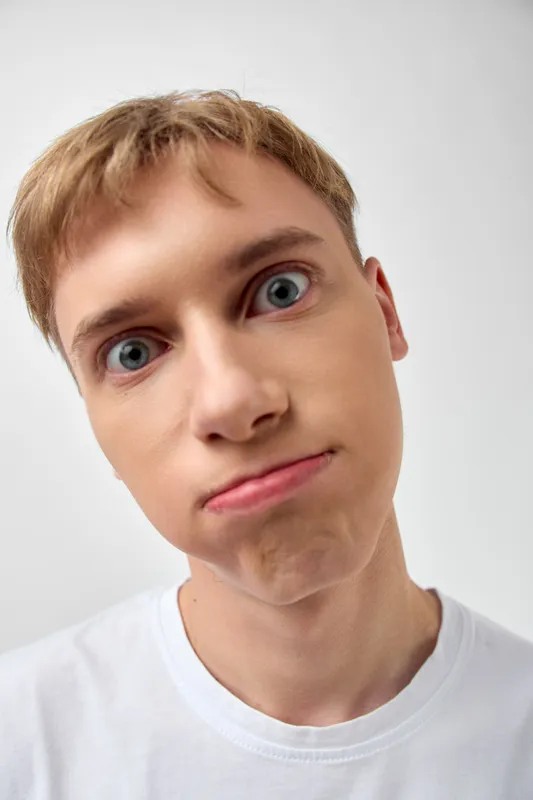 Silly expression close up face boy wide-eyed quirky mood humorous posture playful grin bright skin short hair tshirt background studio shot facial features cheeky look expressive gaze youthful pose