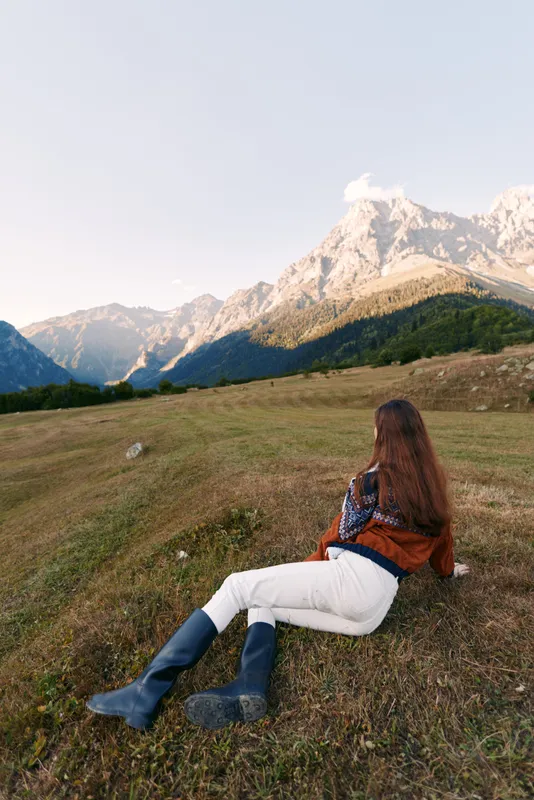 Woman lying on grass in a mountain meadow, boots visible, peaceful landscape and nature scene for outdoor relaxation, travel and scenic summit view at golden hour.