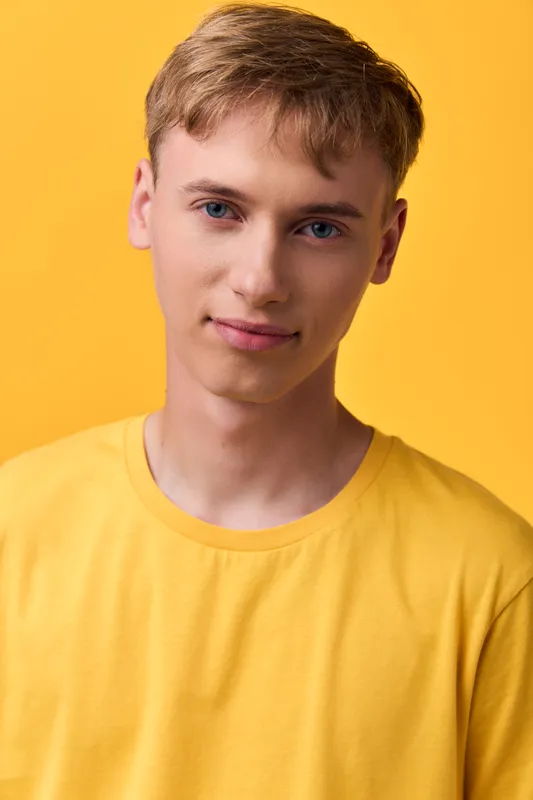 Young man in a yellow shirt stands in a studio with soft lighting, casual pose and relaxed expression, a clean modern fashion shot for lifestyle, branding and product presentation