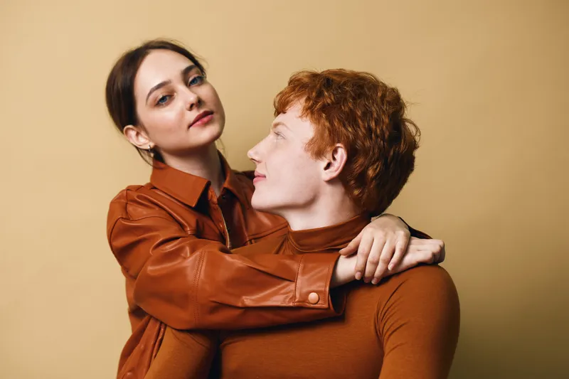 Couple, woman and man embracing and posing on beige background. Young adults with casual clothes and tender facial expressions standing close in studio portrait.