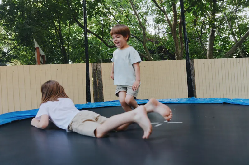 Joyful children playing on a trampoline, enjoying their summer day outdoors in a lively, green backyard setting.