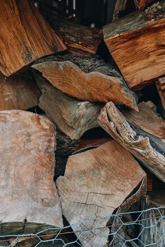 Firewood stacked logs and split logs in a rustic wood pile, natural texture closeup with chicken wire. Outdoor backyard fuel, cozy cabin atmosphere and winter preparation for heating.