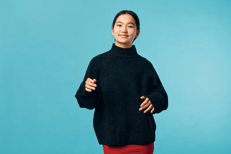 Young woman in black sweater and red skirt posing with smiling face on blue background, casual style and confident expression for lifestyle and fashion portrait.