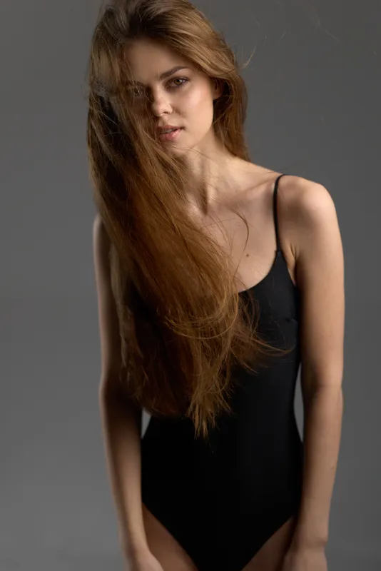 Young woman with long flowing hair wearing black sleeveless dress against grey background