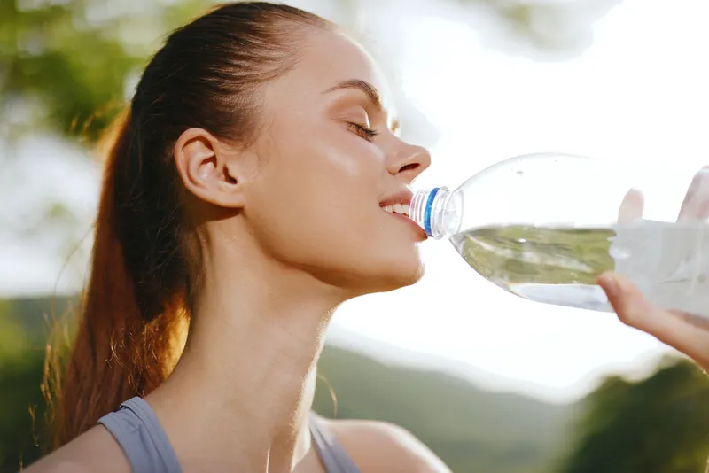 Young woman enjoying refreshing water in nature, promoting healthy hydration and fitness lifestyle, captured in a vibrant outdoor setting