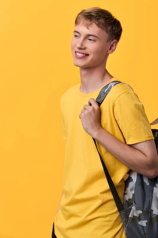 Smiling student wearing a yellow shirt with a camouflage backpack against a bright backdrop, casual fashion and youthful energy for study, travel and daily adventures