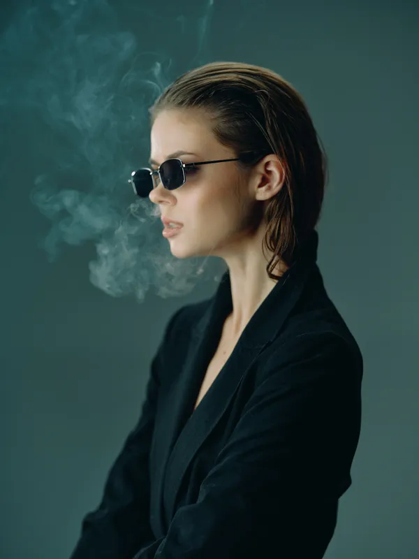 Stylish woman with sunglasses and wet hair in dark outfit with smoke on dark background
