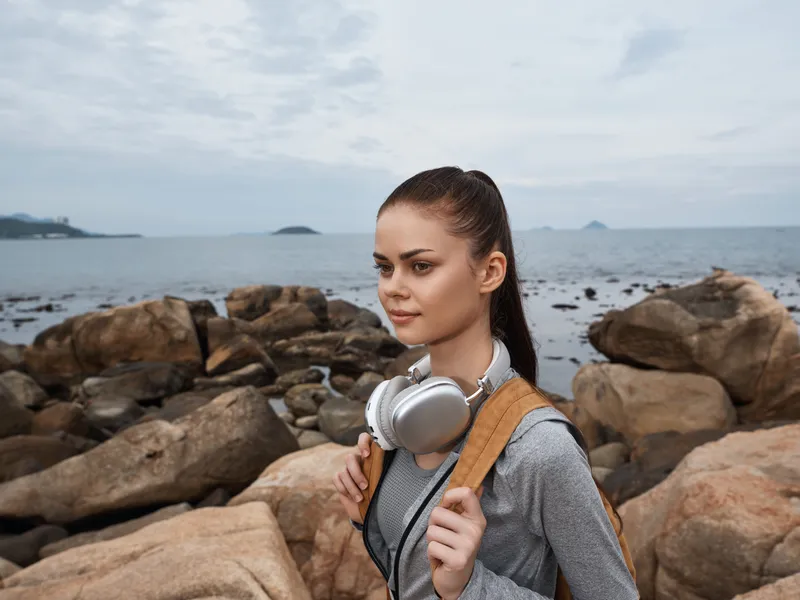 Young woman enjoying nature by the seaside, wearing casual sportswear and headphones, with an adventurous expression amidst rocky coastline