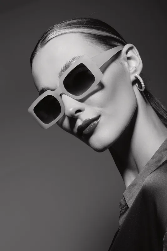 Young caucasian woman with pale skin wearing large sunglasses and earrings in minimalistic studio. Concept of fashion, style, and modern accessories.