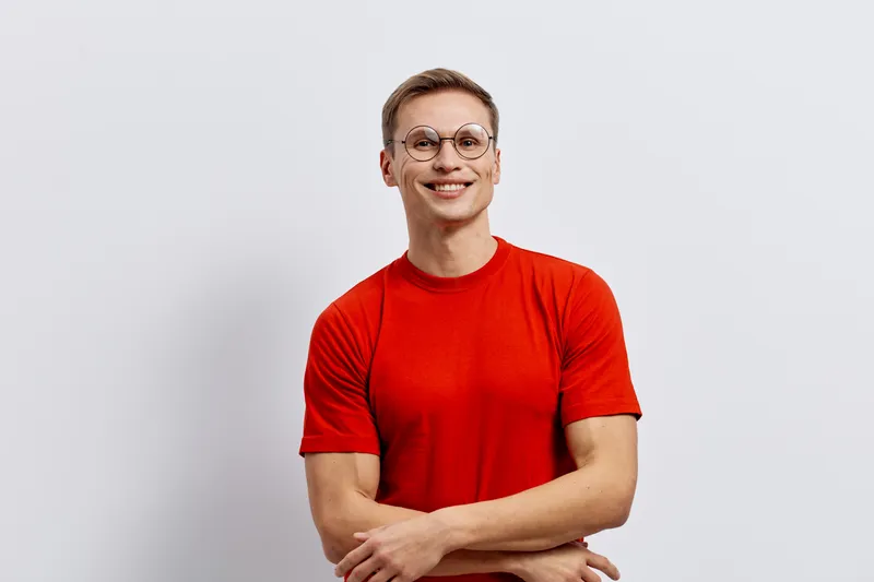 Smiling young caucasian man wearing red t-shirt round glasses look camera standing arms crossed white background digital detox mental health concept