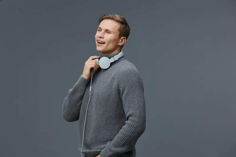 Smiling young man with headphones gray sweater gray background enjoying music mental health and gadgets concept positive emotion portrait