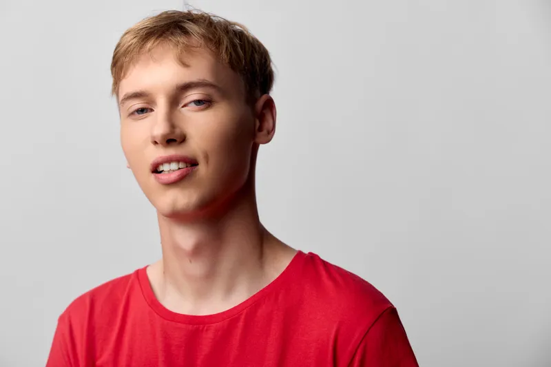 Young man in a red shirt stands against a neutral studio backdrop, presenting a clean, fashionable look suitable for stock, lifestyle, and product showcase projects in ecommerce contexts