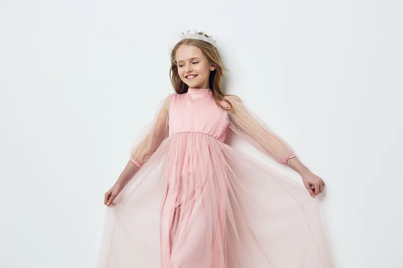 Young girl in a pink dress with tulle sleeves, showcasing joy and elegance against a soft, neutral background, ideal for seasonal fashion or children s portraits