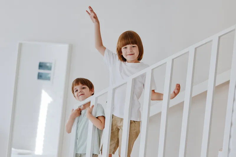 Two cheerful boys playfully climbing stairs in a modern home, smiling and enjoying their time together. Bright and inviting atmosphere enhances their joy.