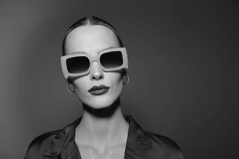 Blonde caucasian woman with pale skin wearing oversized sunglasses and hoop earrings in a studio portrait.