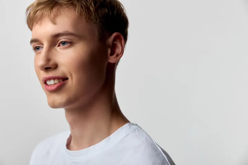 Smiling young man in a white shirt in a studio with soft light, clean background and casual vibe, highlighting a friendly expression perfect for lifestyle or fashion related projects