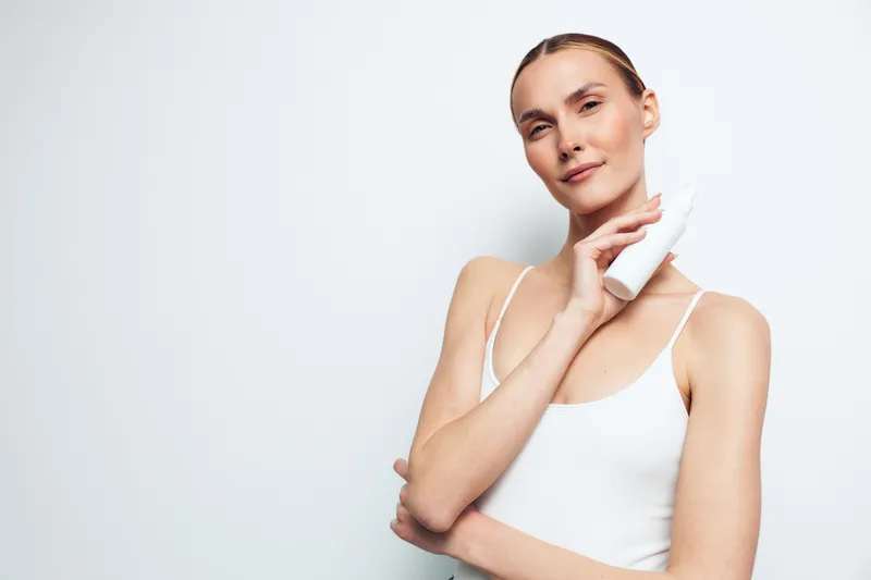 Clear portrait of a woman applying moisturizer to her neck, soft lighting, clean white background, natural skin tone, calm expression, simple beauty routine moment, fresh look