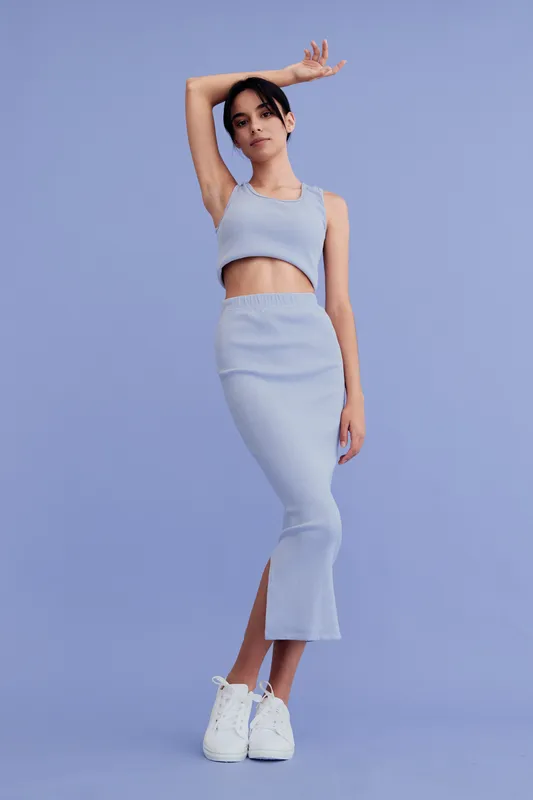 slender woman posing in light blue knit top and skirt with white sneakers against blue background, stylish casual outfit, youthful and modern look