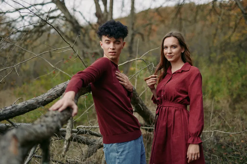 A candid duo stands beside a weathered fence in warm autumn tones, conveying a genuine moment and quiet connection between companions in a natural setting.