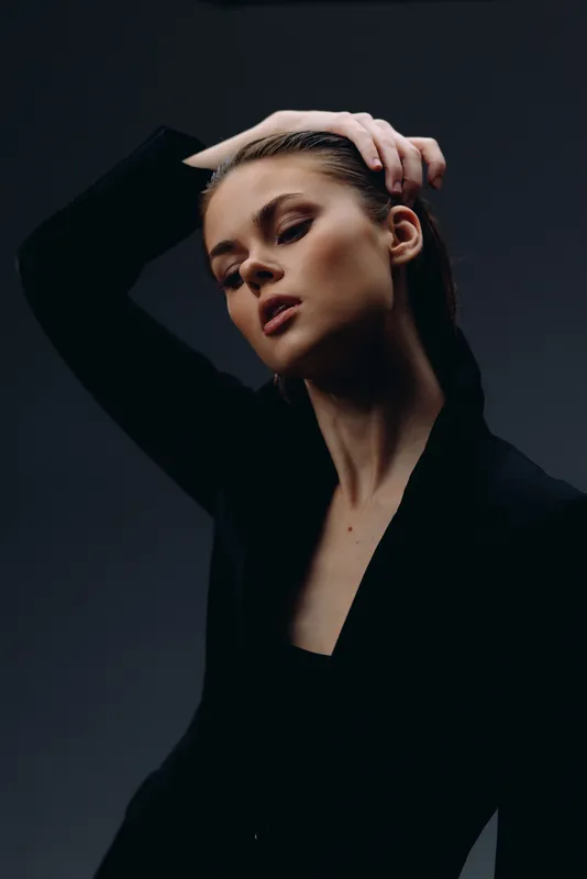 elegant woman posing with hand on head in dark moody lighting, fashion portrait style