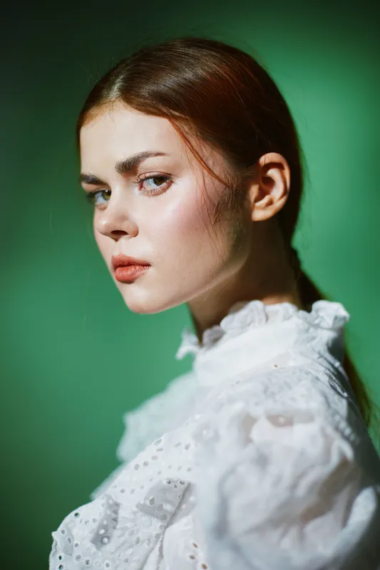 Portrait of a young woman with a serene expression, wearing a white vintage blouse, against a soft green background, capturing beauty and elegance