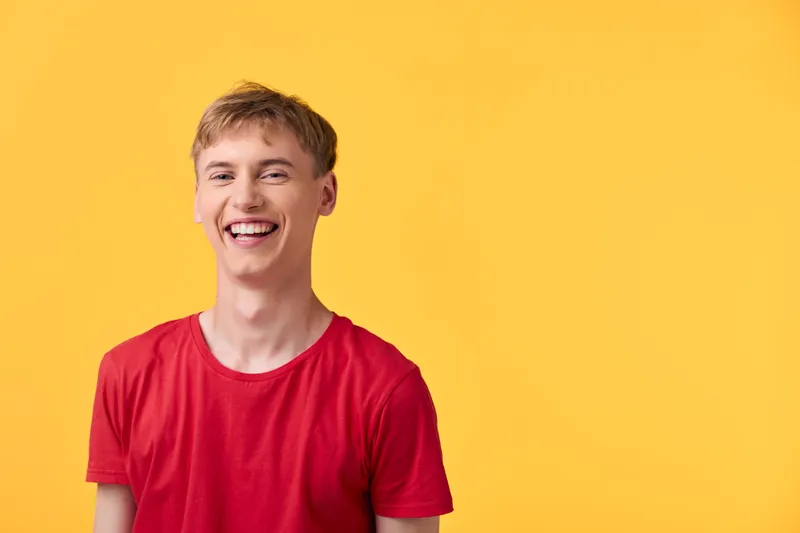Happy man with a smile wearing a red shirt stands against a yellow background in a studio, conveying casual fashion, upbeat mood, and confident energy and success